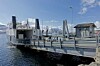 Bildet viser MF Helgøy, ved brygga i Hansnes, med Reinøya på andre siden av sundet. Bildet er tatt 6. mai 2019, en solrik dag på våren i Nord-Norge.