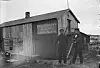 To menn fotografert foran 'Jørgensens Etablissement. Kjøb og Salg. Fiskeprodukter - Handelsvarer'. Bildet skal være tatt på Hansholmen i Sklinna i 1906.