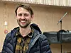Smilende mann i mørk jakke foran mikrofonstativ og keyboard i kirken.