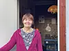 Smilende kvinne i rosa cardigan står i en åpen døråpning.