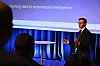 Jakob Mo står på en opplyst scene og presenterer foran en projisert lysbildeserie.