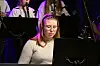 Musiker ved et piano med orkester og notestativer i bakgrunnen.