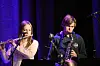 To musikere spiller fløyte og saksofon på en scene med fiolett lys.