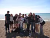 Gruppe unge mennesker poserer på en strand ved havet.