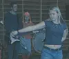 Tre unge musikere med gitar og trommer i et dunkelt øvingslokale.