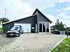 Mørk moderne bygning med glassinngang, biler og brosteinsbelagt gårdsplass under blå himmel.