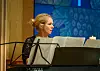 Kvinnelig musiker ved et Kawai-klaver med noter foran et blått dekorativt bakteppe.