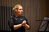 Kvinnelig sanger i svart står ved et notestativ i en konsertsal.