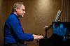 Pianist spiller på et svart Yamaha-flygel i et trepanelert rom.