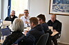 Gruppe voksne sitter samlet rundt et konferansebord med laptop og dokumenter.