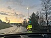 Våt vei med bil, lysregulering og et gult veiarbeidsskilt i et boligområde.