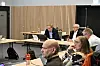 Flere personer sitter rundt bord i et møterom under et kommunalt møte.