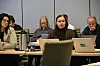 Personer sitter rundt et møtebord med bærbare datamaskiner og dokumenter.